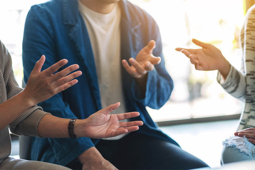 Een paar mensen zijn met elkaar gesprek. Je ziet alleen de handen die handgebaren maken.